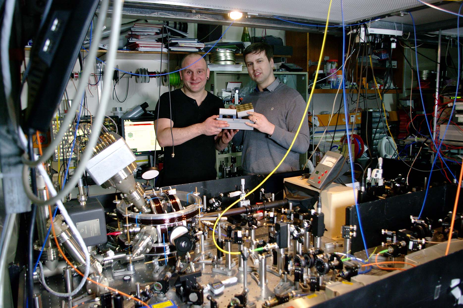 Prof. Hensinger (left) and Dr Lekitsch (right) with a quantum computer blueprint model behind a quantum computer prototype at the University of Sussex.