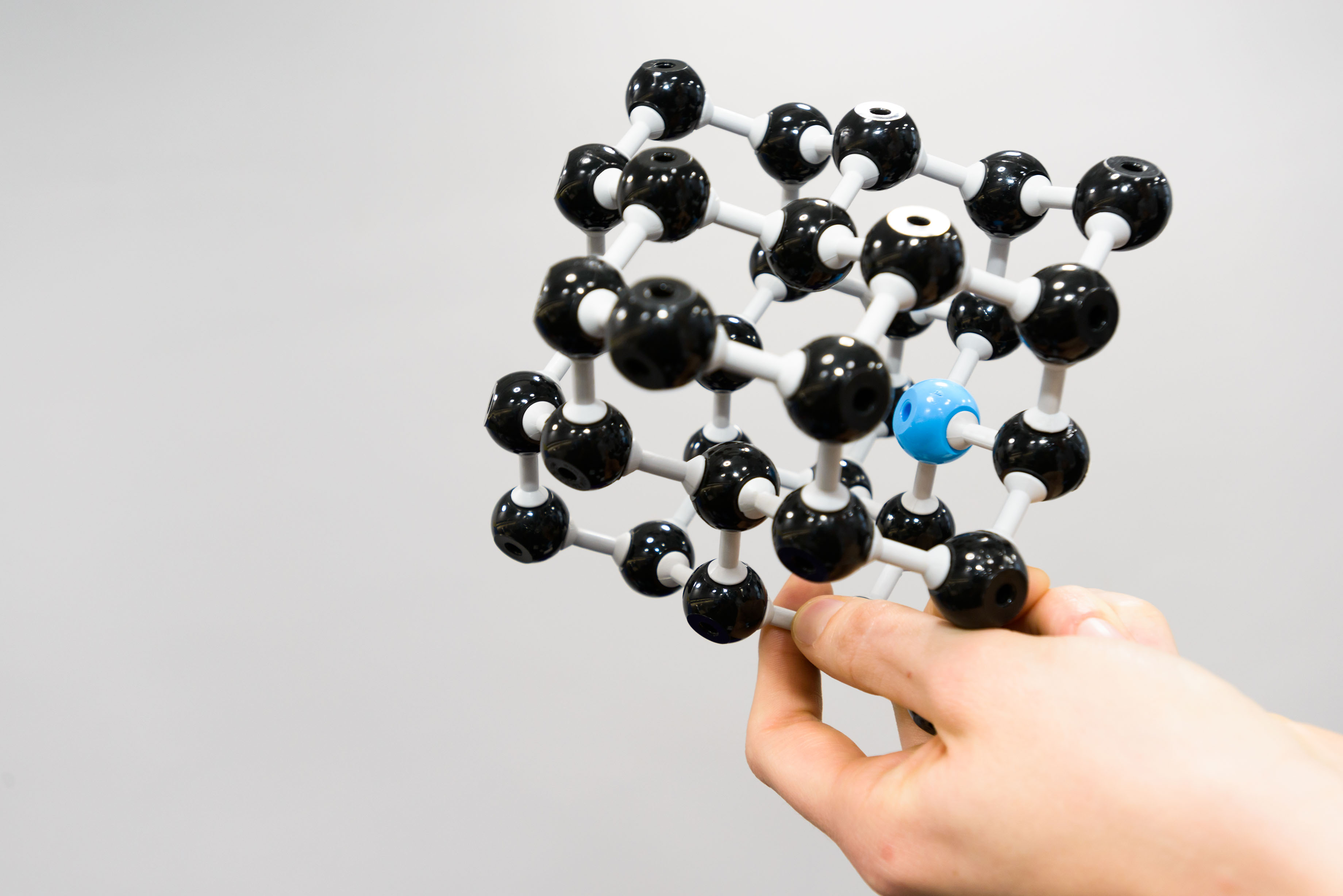 A model of a diamond lattice, with carbon atoms in black and an “NV” centre represented by a blue nitrogen atom next to a gap in the lattice. Credit: Dan Tsantilis / EPSRC